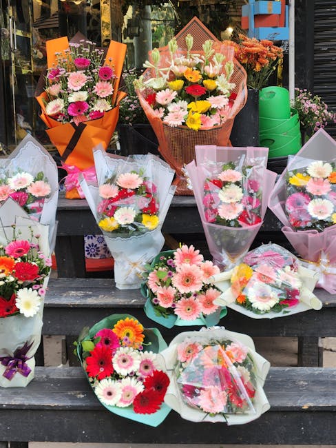 A display of various floral bouquets arranged on outdoor wooden steps, showcasing a mix of fresh flowers including pink, white, yellow, and red gerbera daisies, chrysanthemums, and roses. The bouquets
